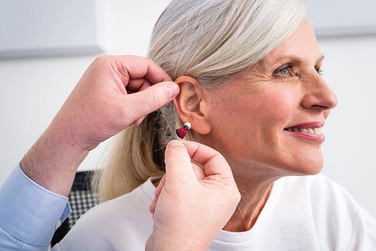 Ältere Frau erhält ein Hörgerät, Hörakustiker passt modernes Hörsystem am Ohr an.